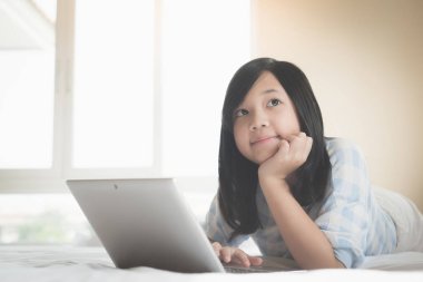 Yatakta yatan ve beyaz yatakta dizüstü kullanarak şirin Asyalı kız