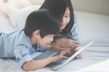 Yatakta yatan ve beyaz yatakta dizüstü kullanarak sevimli Asya çocuk