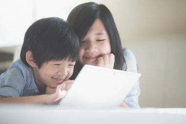 Yatakta yatan ve beyaz yatakta dizüstü kullanarak sevimli Asya çocuk