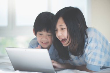 Yatakta yatan ve beyaz yatakta dizüstü kullanarak sevimli Asya çocuk