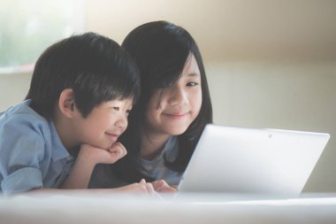 Yatakta yatan ve beyaz yatakta dizüstü kullanarak sevimli Asya çocuk