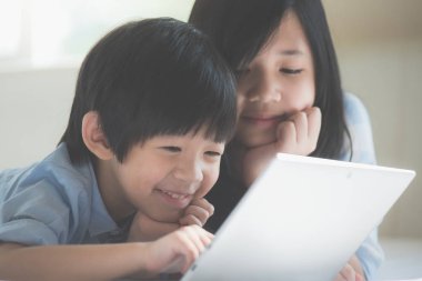 Yatakta yatan ve beyaz yatakta dizüstü kullanarak sevimli Asya çocuk