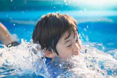 Tatlı Asyalı çocuk yüzüyor ve havuzda oynuyor.