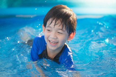 Tatlı Asyalı çocuk yüzüyor ve havuzda oynuyor.