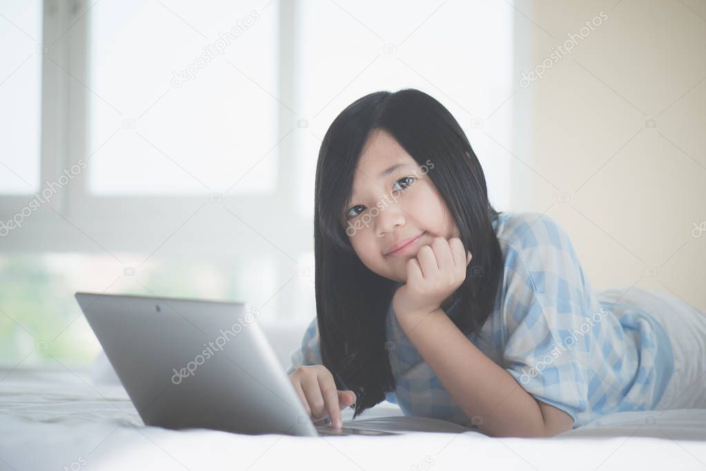 Cute Asian girl lying in bed and using laptop on white bed