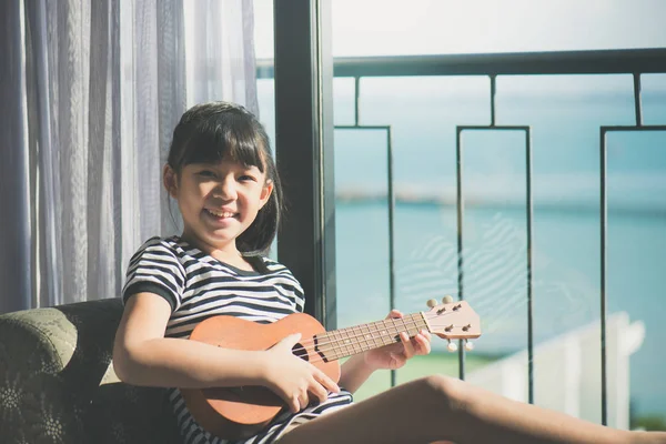 亚洲女孩与海面背景窗口附近玩夏威夷四弦琴 — 图库照片