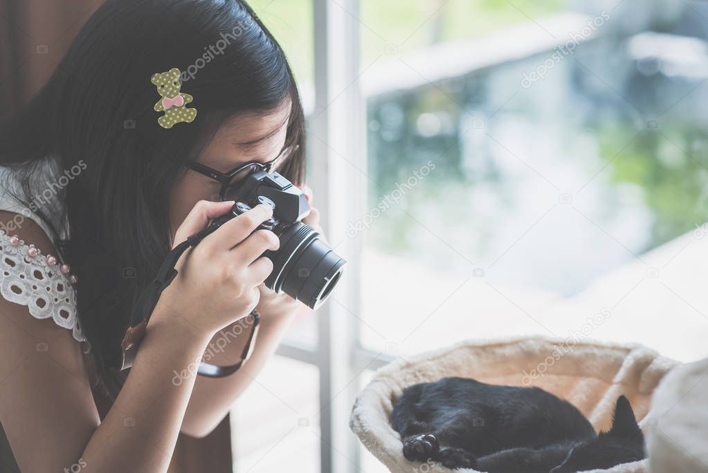 Asian Girl taking a photo of black kitten sleeping on cat tower