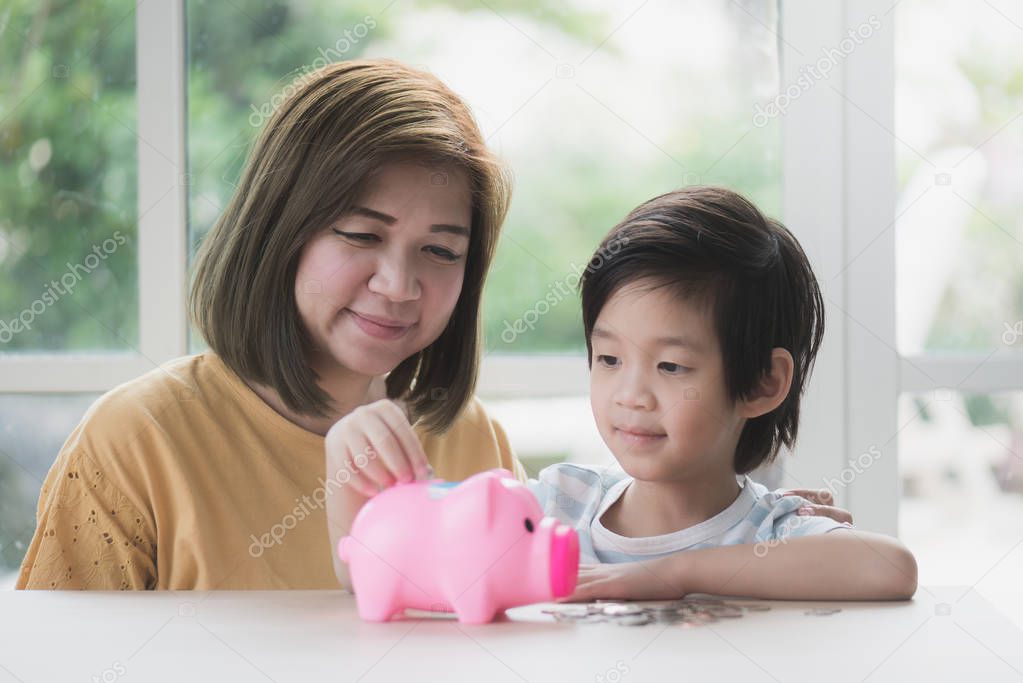 Cute Asian child putting a coin into a piggy bank