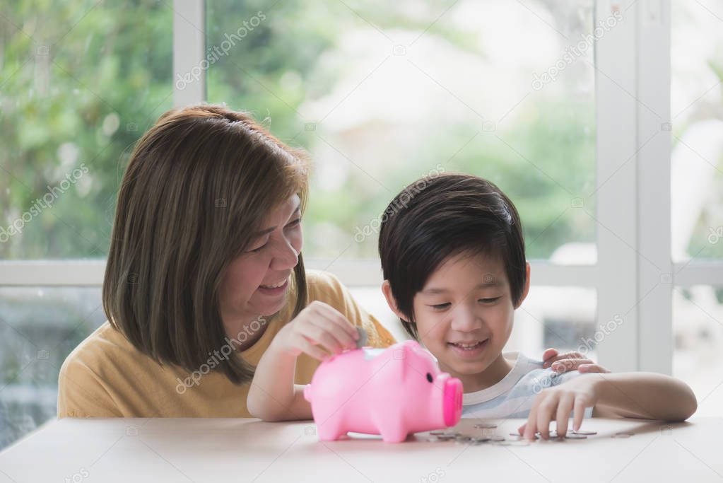 Cute Asian child putting a coin into a piggy bank