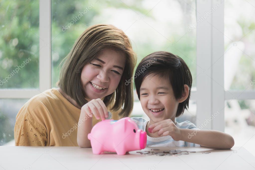 Cute Asian child putting a coin into a piggy bank