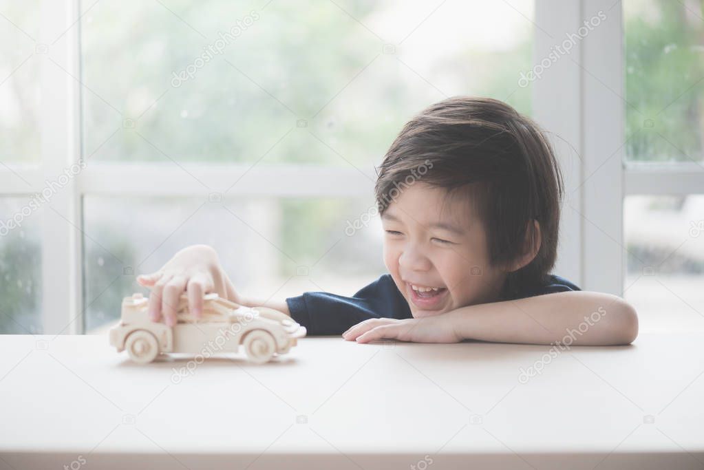 Cute Asian child playing wooden model car on a table
