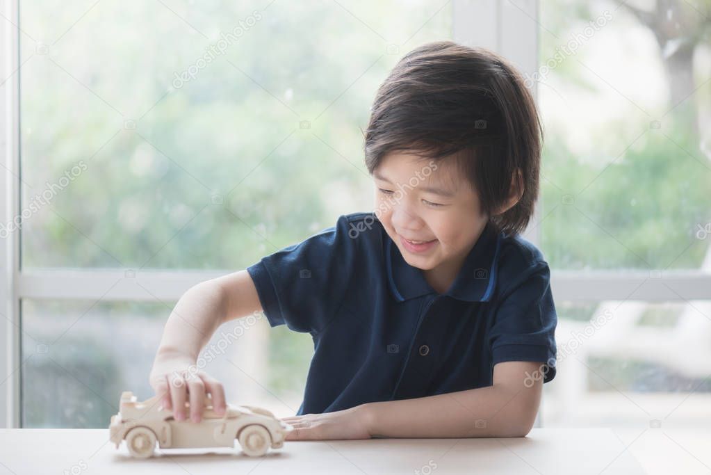 Cute Asian child playing wooden model car on a table