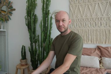 Yatakta oturan kel genç bir adam. Yeşil gömlekli adam.