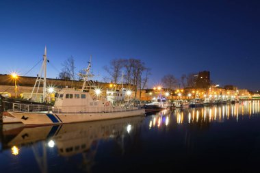 Litvanya 'nın Klaipeda şehrinde gün batımında tekne ve yatlar için rıhtım. Damarların güzel manzarası ve mavi saatte sakin sulardaki yansımaları.