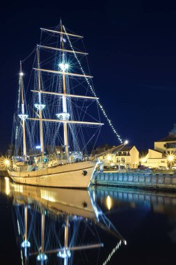 Yelkenli teknesi Litvanya 'nın eski Klaipeda kasabasında demir attı ve gece ışıkları açıktı. Ortaçağ kasabası ve barquentine sakin sularda yansıması.