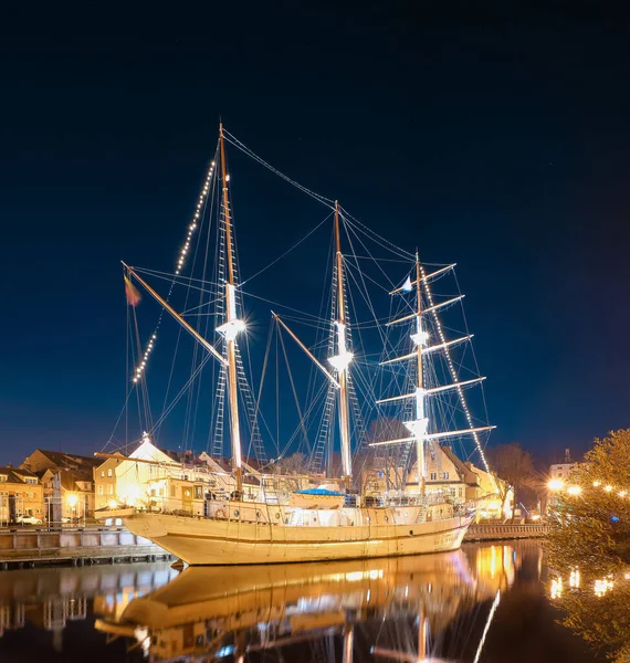 Segelboot ankert in der Altstadt von Klaipeda, Litauen, bei eingeschaltetem Abendlicht. Mittelalterliche Stadt und barquentinische Spiegelung in ruhigen Gewässern. — Stockfoto