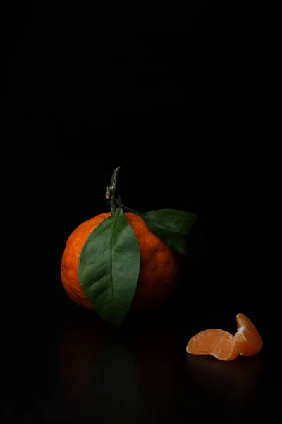 Mandarin med gröna blad och skivor av mandarin isolerad på svart bakgrund. Vertikal bild — Stockfoto