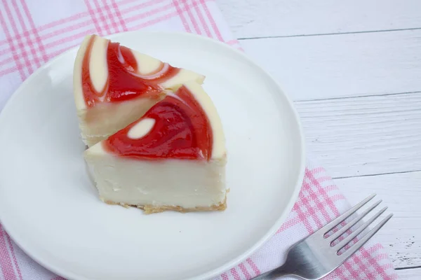 Two pieces of cheesecake on a plate and a fork on tablecloths on white wooden background flat lay — Stock Photo, Image