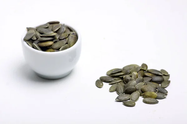 Una ciotola e un mucchio di semi di zucca isolati su sfondo bianco posa piatta. Immagine orizzontale — Foto Stock