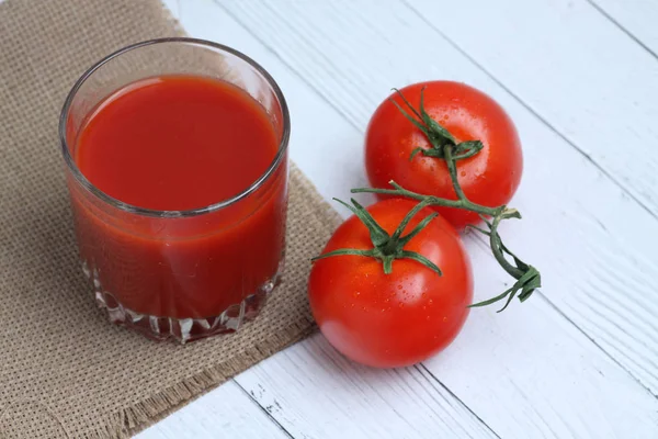 Um copo de suco de tomate e tomates na toalha de mesa de lona no fundo de madeira branca flat lay. Imagem horizontal — Fotografia de Stock