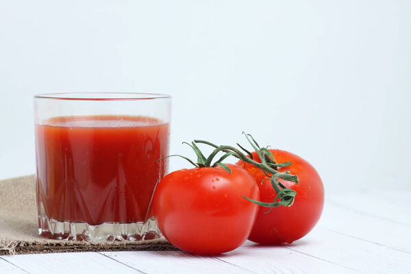 a glass of tomato juice and tomatoes on canvas tablecloth on white wooden backgrond. Horizontal image