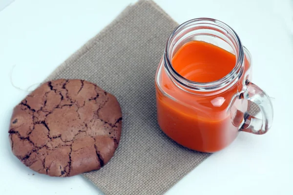 Ποτήρι κούπα χυμό καρότου και ένα μπισκότο σοκολάτας σε χαρτοπετσέτα καμβά που απομονώνονται σε λευκό φόντο επίπεδη lay — Φωτογραφία Αρχείου