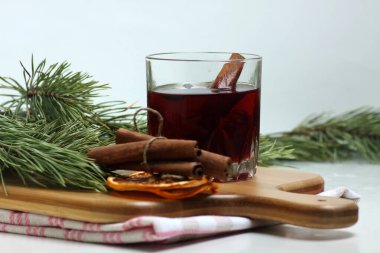 Bir bardak sıcak şarap, tarçın çubukları, portakal parçaları ve köknar dalları beyaz arka planda izole edilmiş kesme tahtasına yakın plan