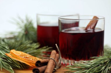 İki bardak sıcak şarap, tarçın çubukları, portakal cipsi ve köknar dalı beyaz arka planda izole edilmiş kesme tahtasında.