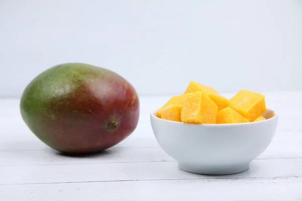 Mango y un tazón de sucesiones de mango sobre fondo de madera blanca — Foto de Stock