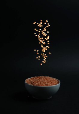red lentils pouring into white bowl on black background