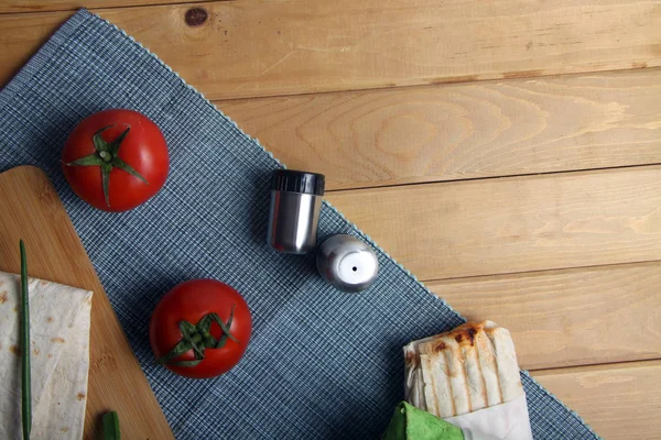 kebap, lavaş kesim tahtasında, domates ve tuzluk tahta zeminde. Resim kopyalama alanı içeriyor