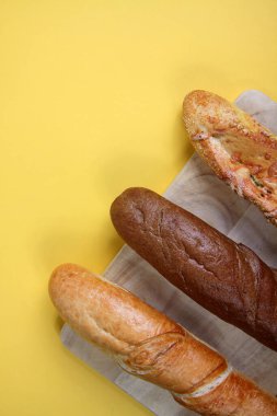 Sarı arka planda, tahta kesme tahtasının üzerinde üç baget. Dikey görüntü. Resim kopyalama alanı içeriyor.