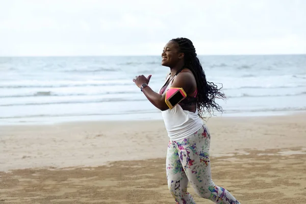 Female african runner jogging during outdoor workout on beach.