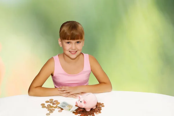 Mała Śliczna Dziewczynka Monetami Świnką Biurku Zielonym Tle Oszczędzanie Pieniędzy — Zdjęcie stockowe