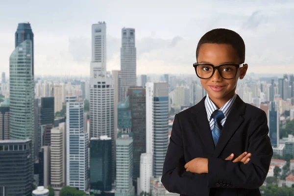 子供の頃と人々は都市を背景にビジネススーツに眼鏡をかけた小さなアフリカ系アメリカ人の少年をコンセプトにした 自信満々の笑顔ポーズ — ストック写真