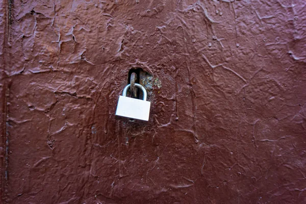 padlock on an old metal door covered in brown paint.