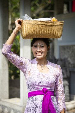 Gülümseyen güzel Balili kadın Endonezya, Bali tapınağındaki tanrılara bir sepet taşıyor.