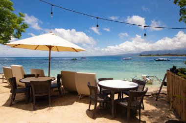 Gili Air, Bali, Endonezya 'da ahşap mobilyaları ve şemsiyeleri olan rahat bir plaj salonu.