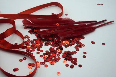 Kırmızı pullar, kırmızı kurdele ve beyaz arka planda kırmızı tüyler. Elbiseleri süslemek için kullanılan dikiş ve dekorasyon aksesuarları