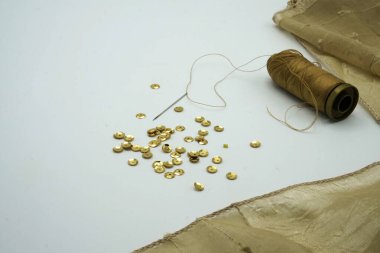 Altın pullar, bir makara altın iplik, dalgalı altın ipekli arka planda iğne. Elbiseleri süslemek için kullanılan dikiş ve dekorasyon aksesuarları.