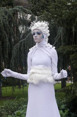 Timisoara, Romanya- 09.06.2019 Kış veya Buz Tanrıçasının Yaşayan Heykeli. Beyaz elbiseli kadın kartopu şapkalı gerçekçi bir insan heykeli gibi poz veriyor..
