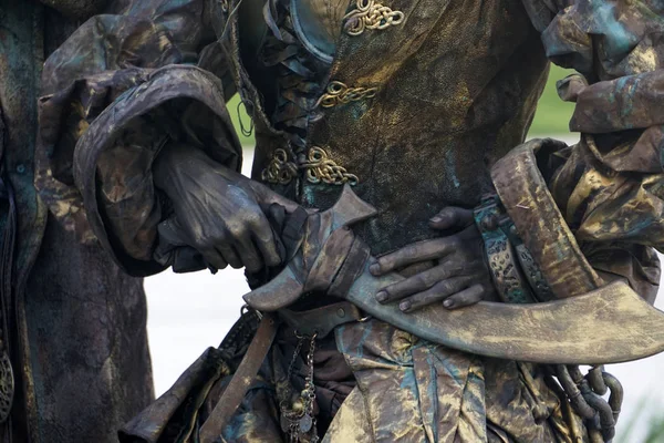 Details of Living statue of two pirates. Woman and man dressed in bronze costumes with hats and weapons pose as a realistic human statue. — Stock Photo, Image