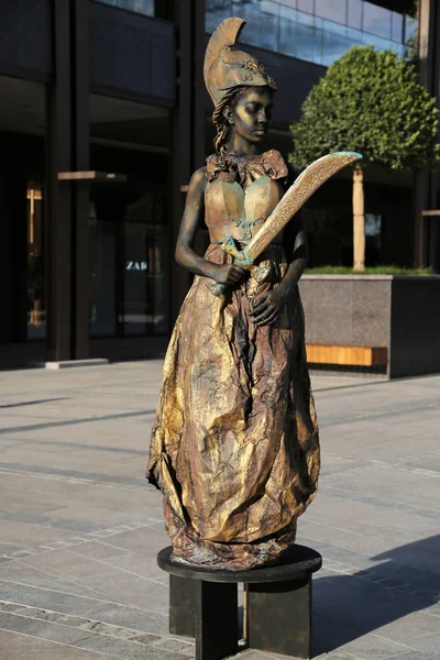 Timisoara, Romania- 09.06.2019 Living statue of Pallas Athena. Woman dressed in bronze dress wearing a helmet and a spear poses as a realistic human statue. — Stock Photo, Image