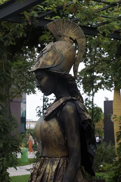 Timisoara, Romania- 09.06.2019 Living statue of Pallas Athena. Woman dressed in bronze dress wearing a helmet and a spear poses as a realistic human statue. — Stock Photo, Image