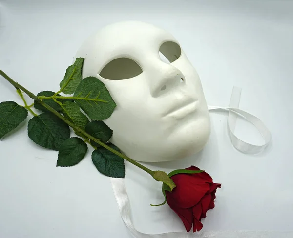 Koncepcja teatralna lub romantyczna. Zbliżenie białej klasycznej maski teatralnej i czerwonej róży jako symbolu wolności seksualnej. — Zdjęcie stockowe