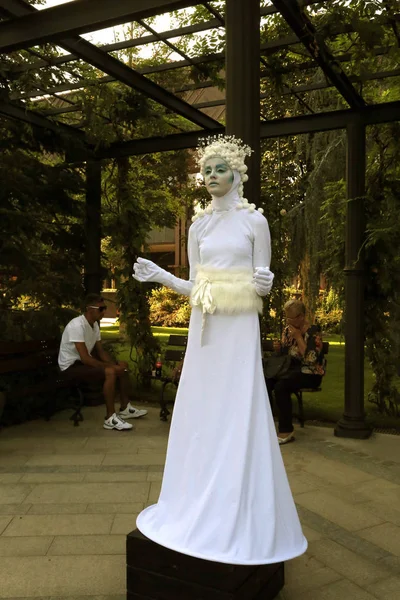 Timisoara, Rumunsko- 09.06.2019 Živá socha bohyně zimy nebo ledu. Žena oblečená v bílých šatech představuje realistickou lidskou sochu v klobouku se sněhovou koulí. Stock Fotografie
