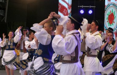 Timisoara, Romanya- 07.04.2019 Dansçılar geleneksel bir Romen halk dansında parktaki ücretsiz festivalde geleneksel güzel kostümler giyerek el ele tutuşuyorlar..