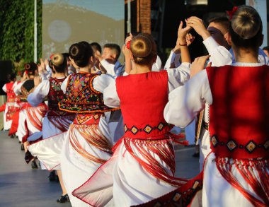 Timisoara, Romanya- 07.04.2019 Dansçılar geleneksel bir Romen halk dansında parktaki ücretsiz festivalde geleneksel güzel kostümler giyerek el ele tutuşuyorlar..