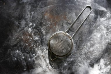 Stainless Steel Fine Mesh Strainer Colander Flour Sieve with Handle on dark background poudered with flour. Kitchenware.