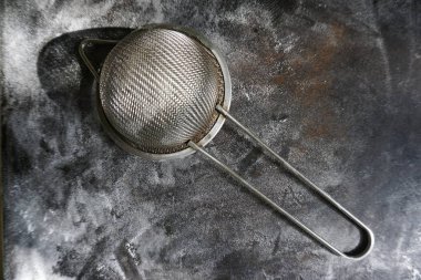 Stainless Steel Fine Mesh Strainer Colander Flour Sieve with Handle on dark background poudered with flour. Kitchenware.